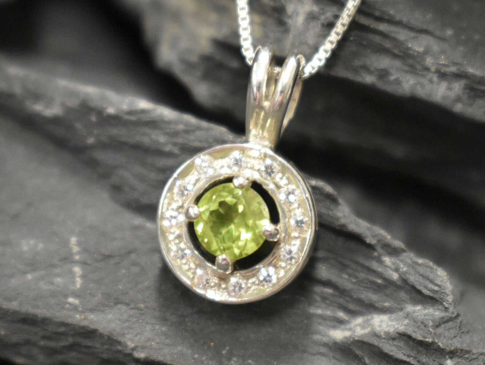 Natural Peridot surrounded by sparkling CZ stones in a round pendant design, known for emotional clarity and perfect for milestone birthdays or anniversaries.