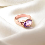 Close-up of rose gold amethyst ring worn on hand showing natural purple gemstone and band