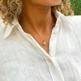 Woman in a white linen shirt, wearing natural opal pendant set in 18k yellow gold over sterling silver. Fire opal necklace ideal gift for her, perfect for wearing solo, and layering necklaces. 