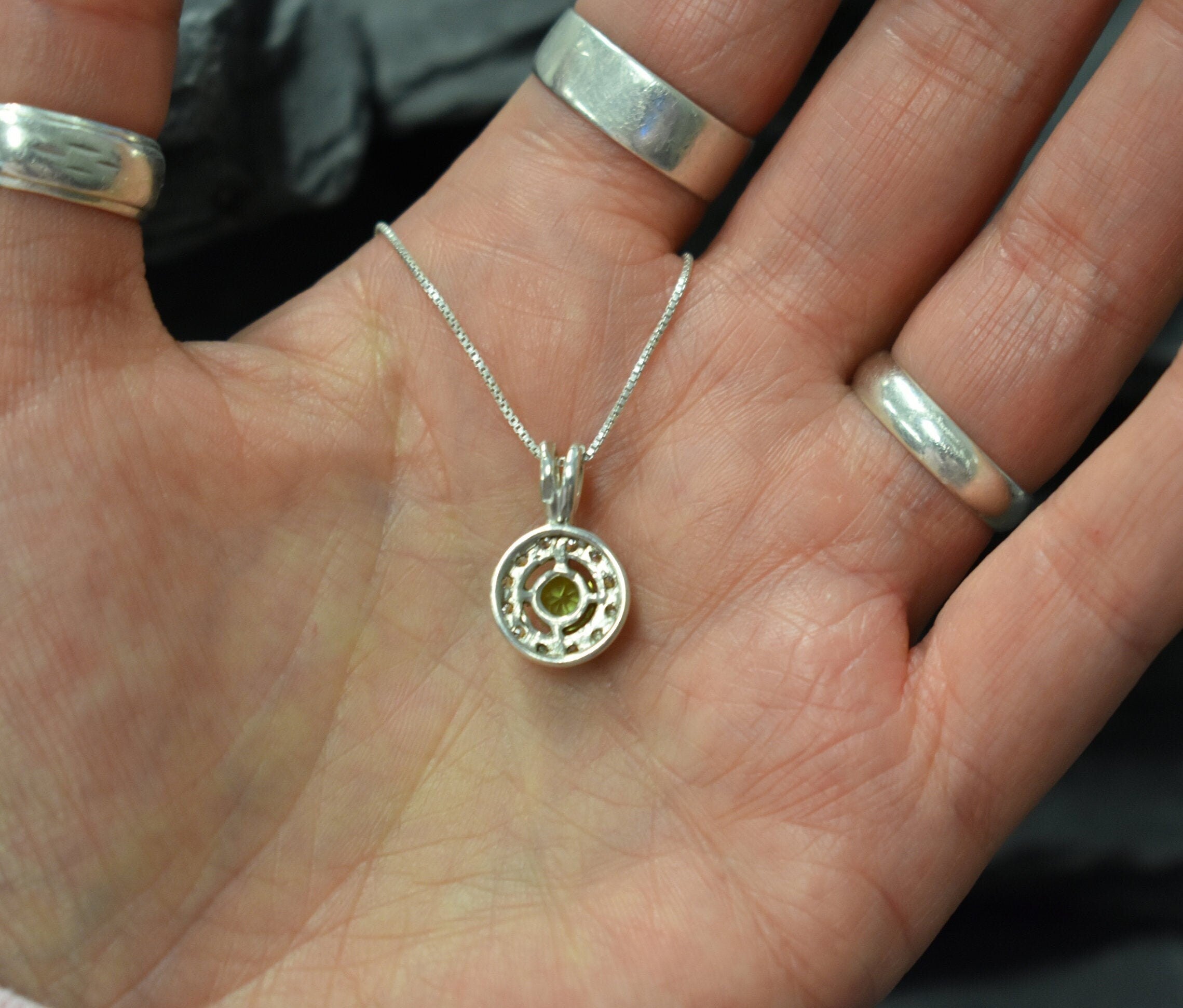 Sparkling green Peridot stone encircled by CZ accents, represents vitality and protection, perfect gift for August babies or gemstone lovers.