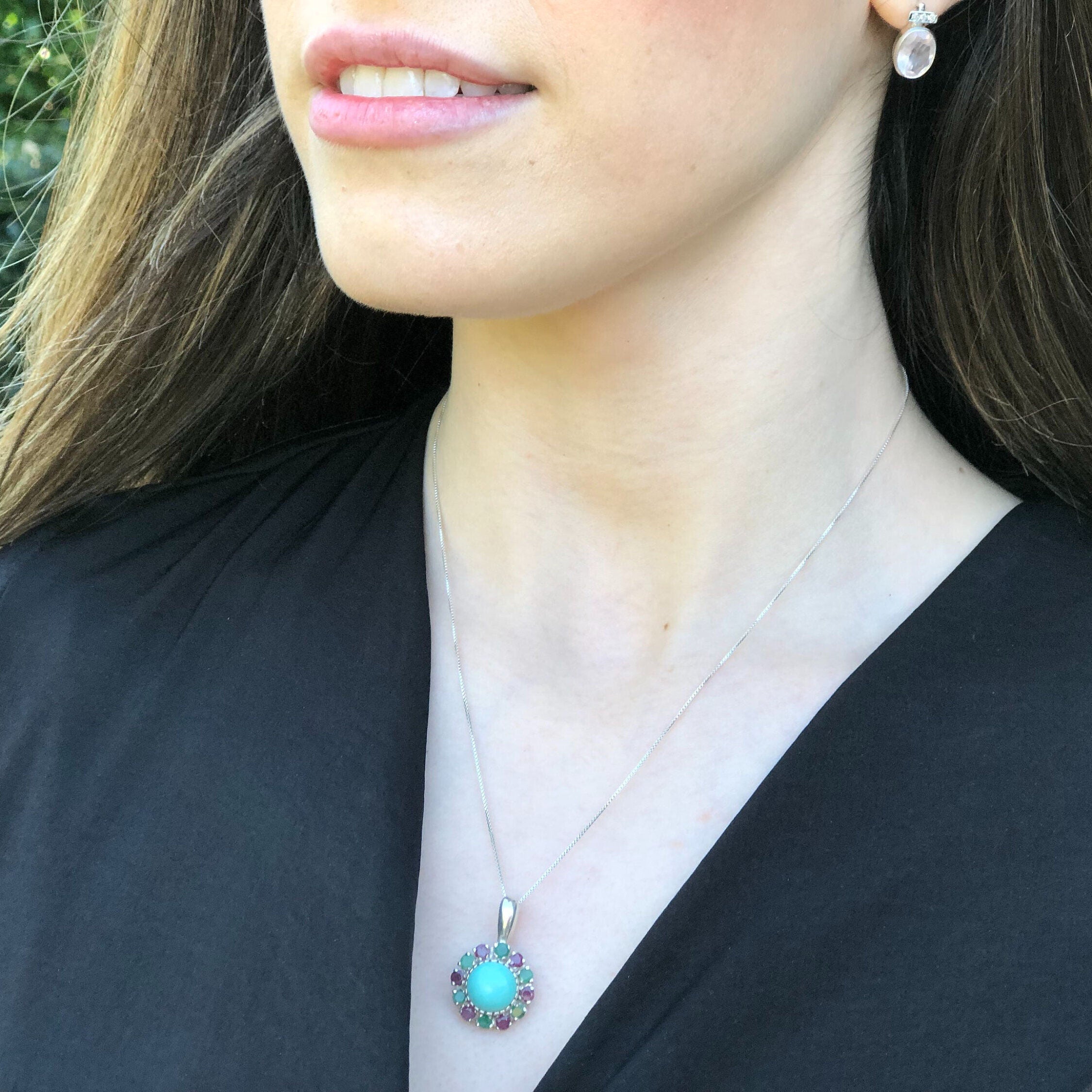 Natural Turquoise pendant with Ruby and Emerald halo styled with a classic black v-neck blouse. The vivid gem colors elevate minimalist outfits and make a thoughtful December birthday gift.