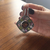 Multistone pendant held gently to show color range, pairs best with dark manicures and neutral-toned outfits for dramatic flair